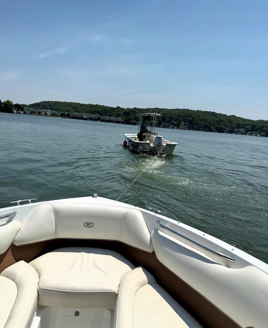 View from a white boat toward a small motorboat on calm water under a clear blue sky.