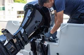 Mechanic adjusting a black outboard motor on a boat docked by a white hull