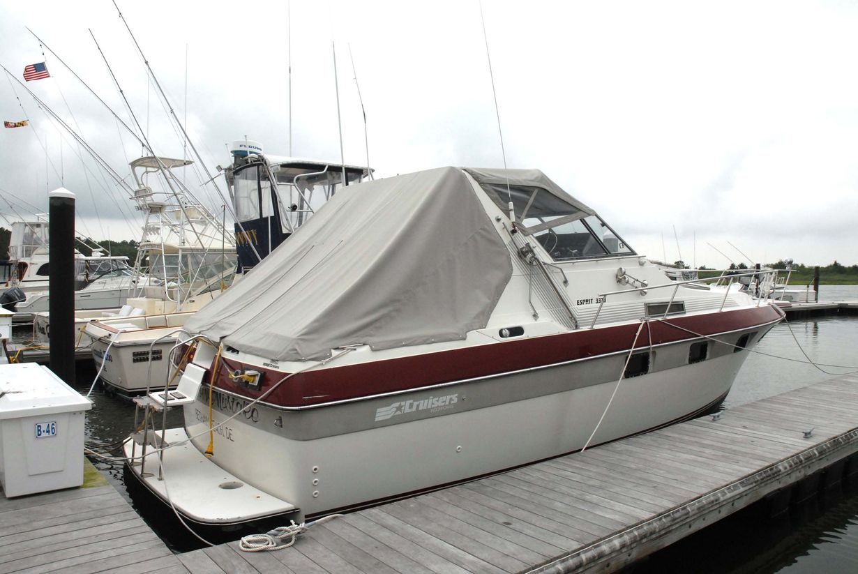 A white and maroon cabin cruiser boat with a tan canvas cover, docked at a wooden pier under a cloudy sky.