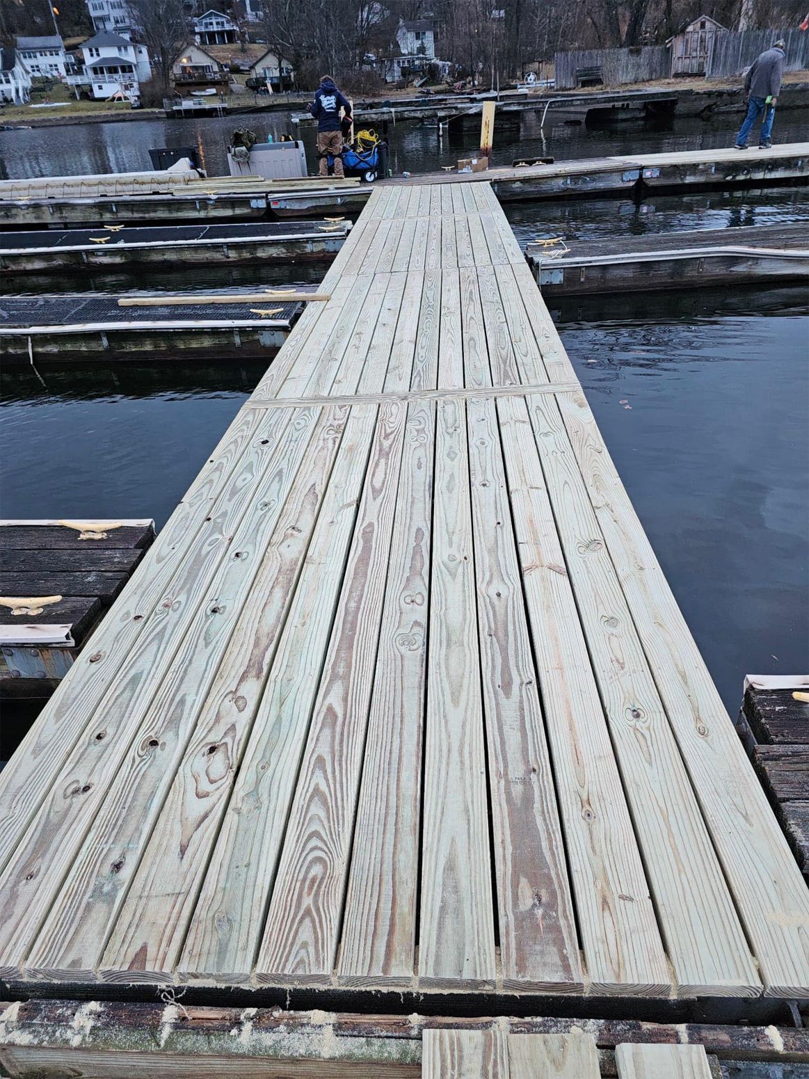 Wooden dock walkway over calm water with snowy shoreline in the background