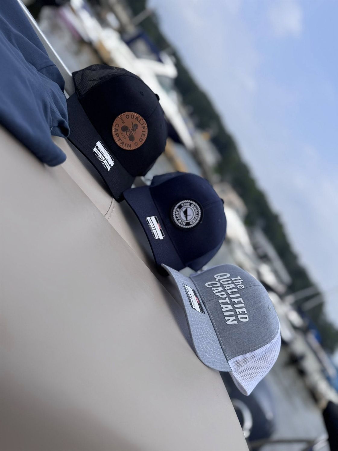 Three baseball caps on a railing outdoors, including a gray cap with white text.