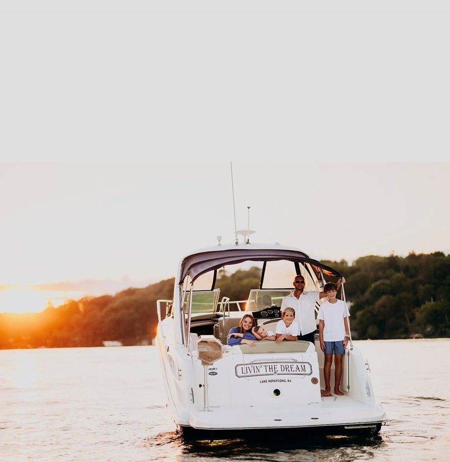 People relaxing on a white boat at sunset on calm water near a tree-lined shore