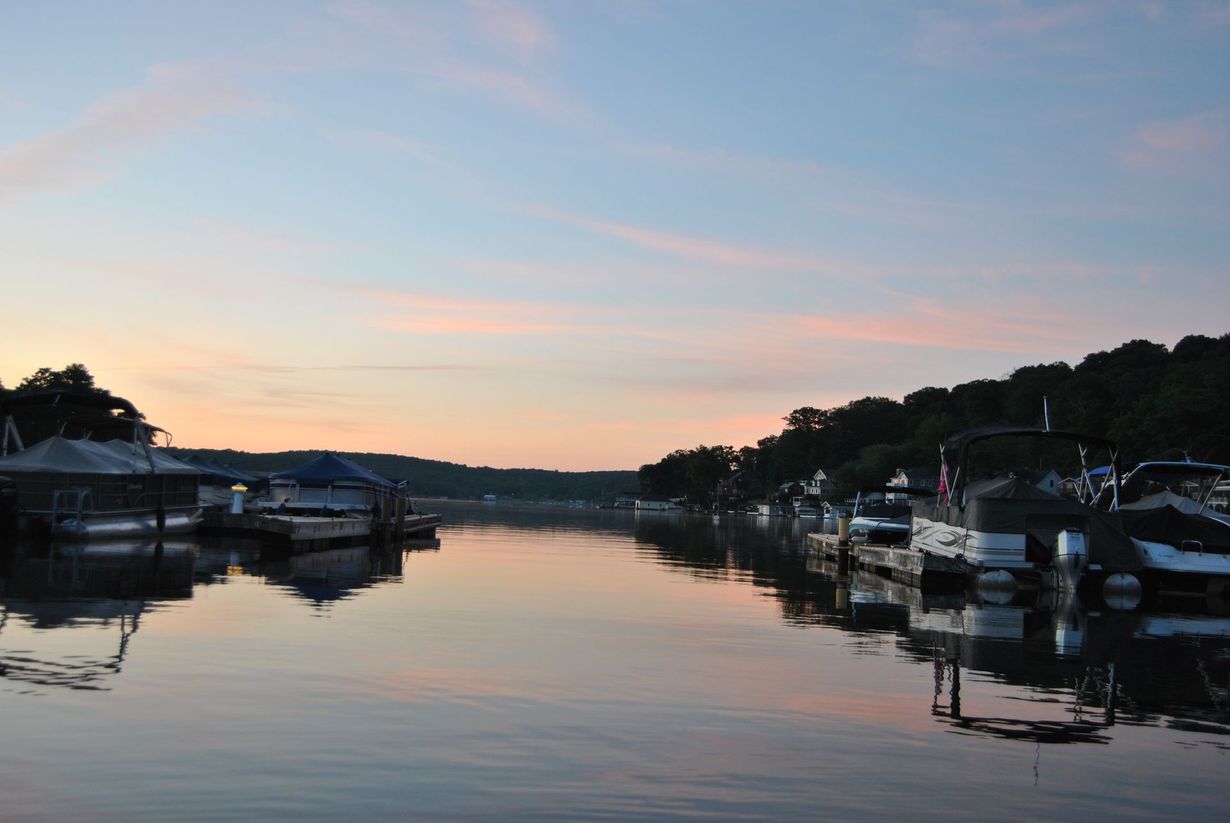 Calm marina at sunset with boats docked along a tree-lined river, reflecting pink and blue sky