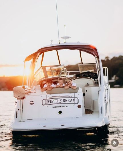White motor yacht at sunset on calm water, viewed from the stern with warm orange light.
