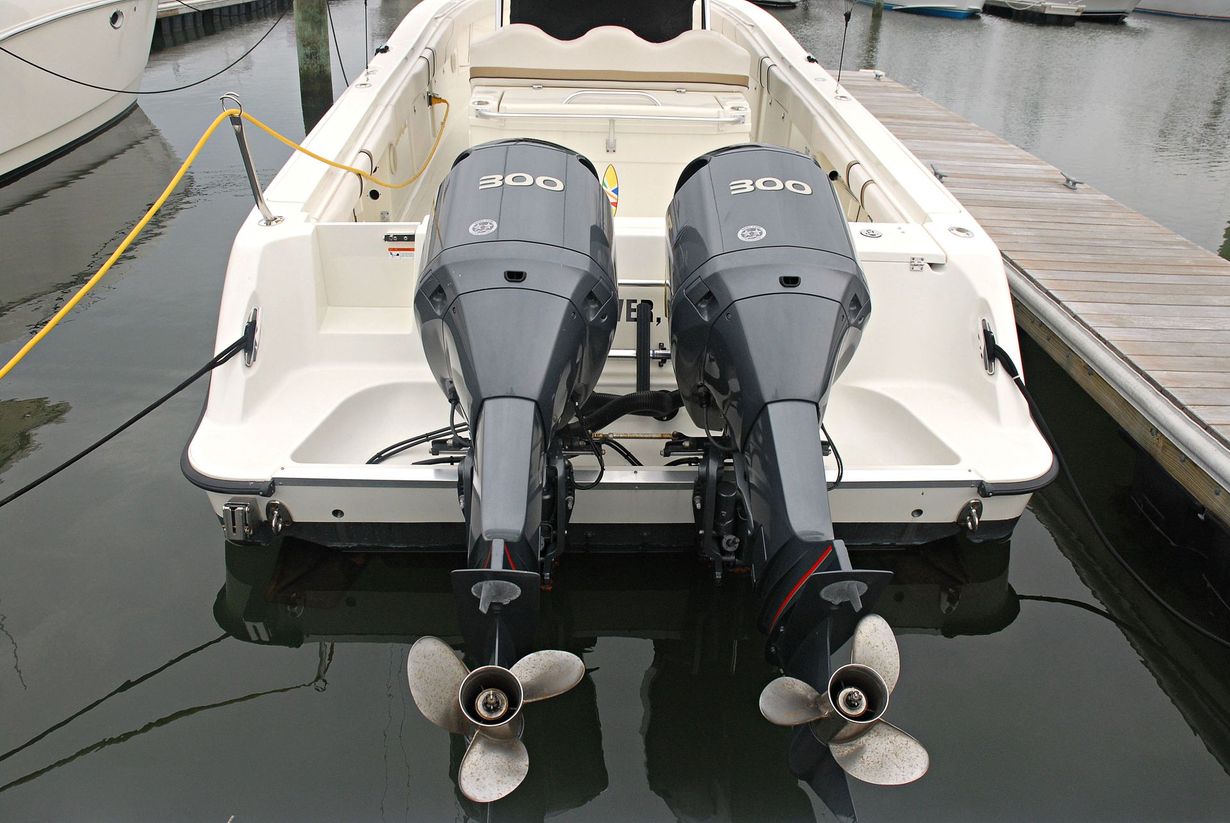 Two gray outboard motors on a white boat docked in calm water.