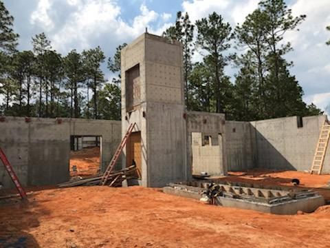 A concrete building is being built in a dirt field with trees in the background.
