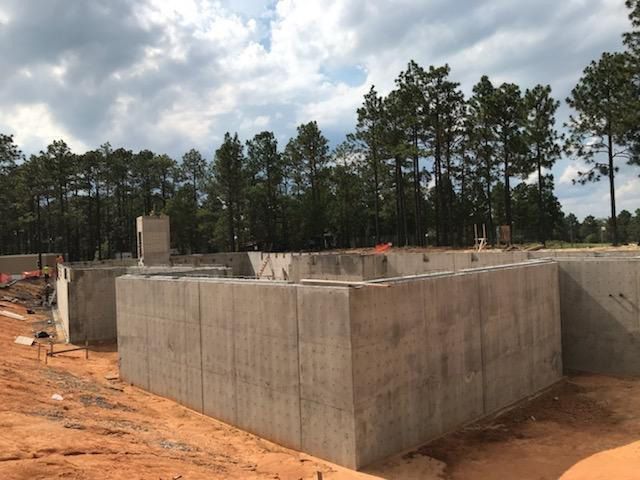 A large concrete wall is being built in a field with trees in the background.