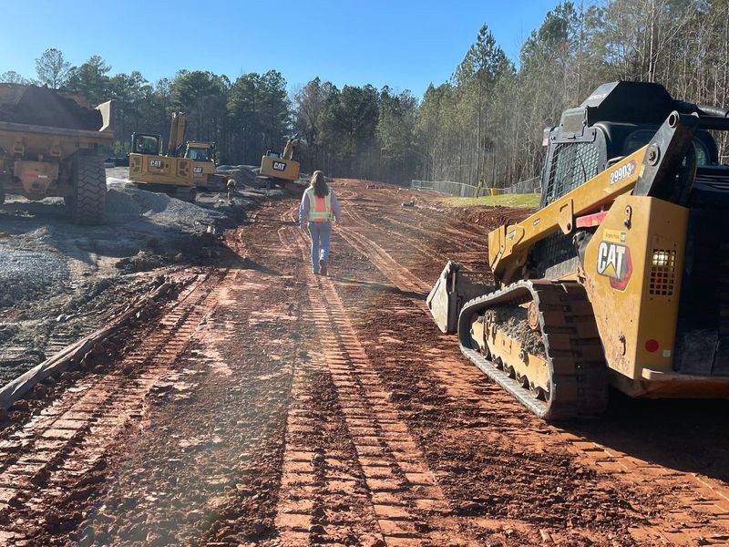 A man is walking down a dirt road next to a cat bulldozer.
