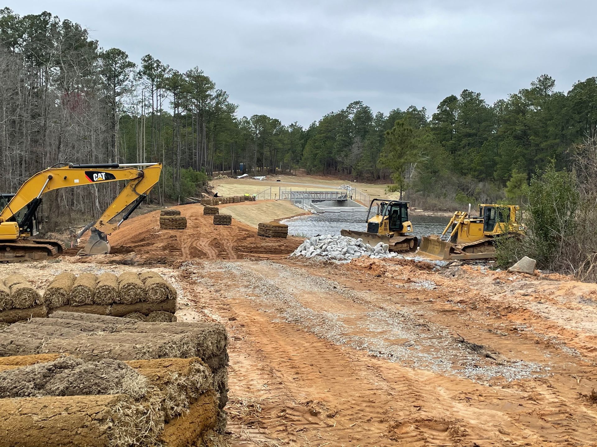 Two bulldozers are working on a dirt road in the woods.
