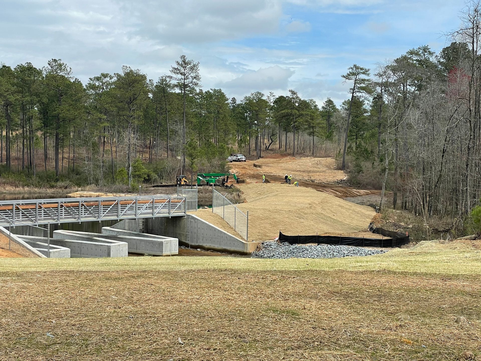 A bridge is being built over a river in a field with trees in the background.