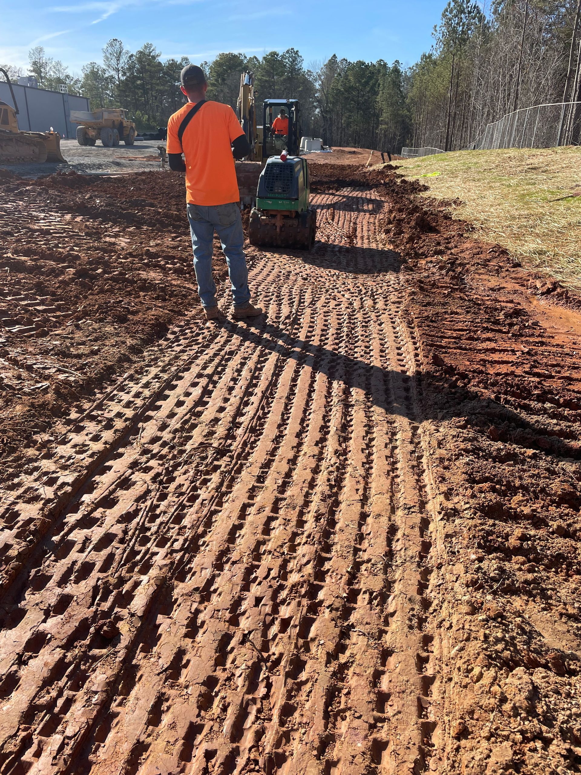 A man in an orange shirt is walking down a dirt road