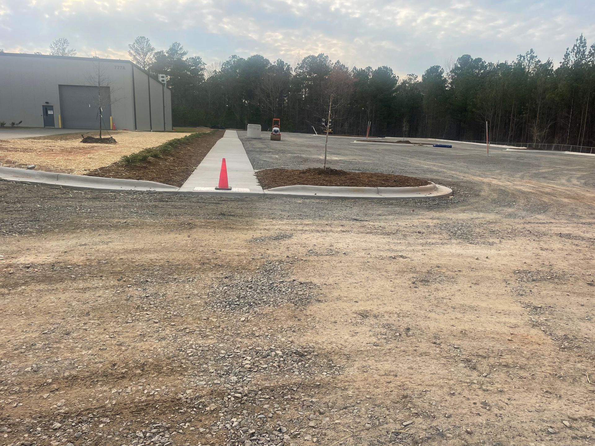 A gravel road with a concrete walkway and an orange cone