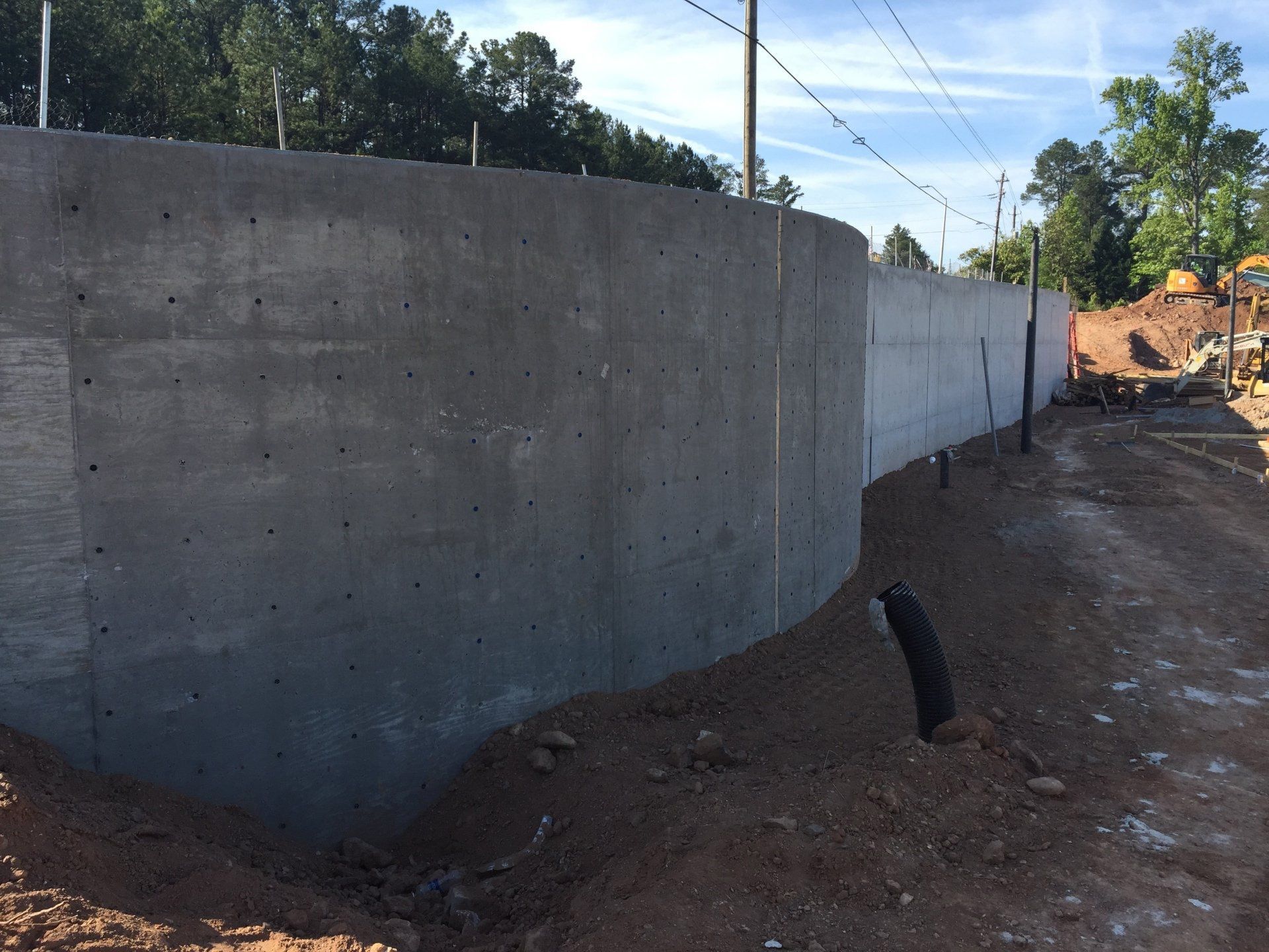 A large concrete wall is being built next to a dirt road.
