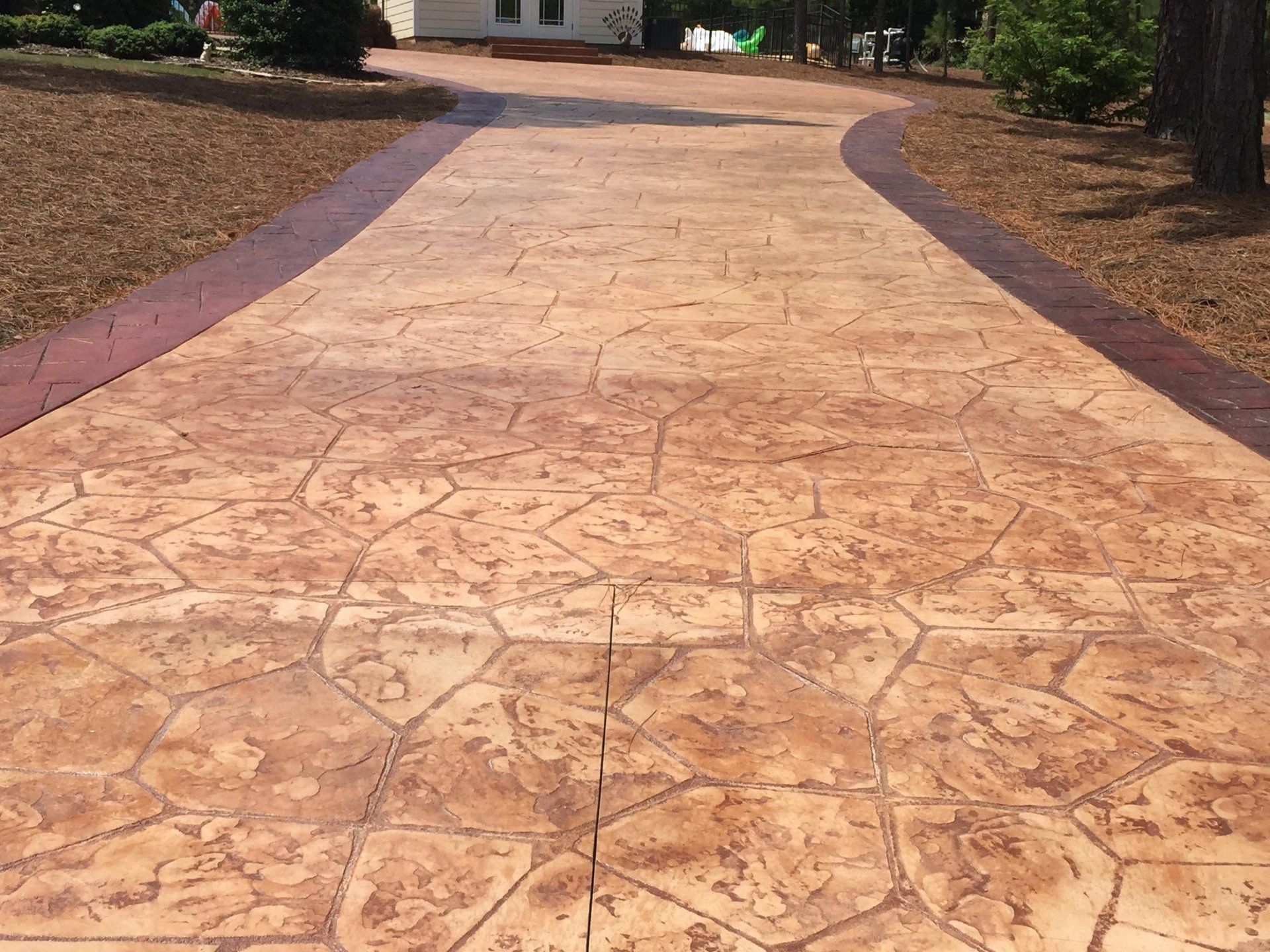 A concrete driveway with a red border leading to a house