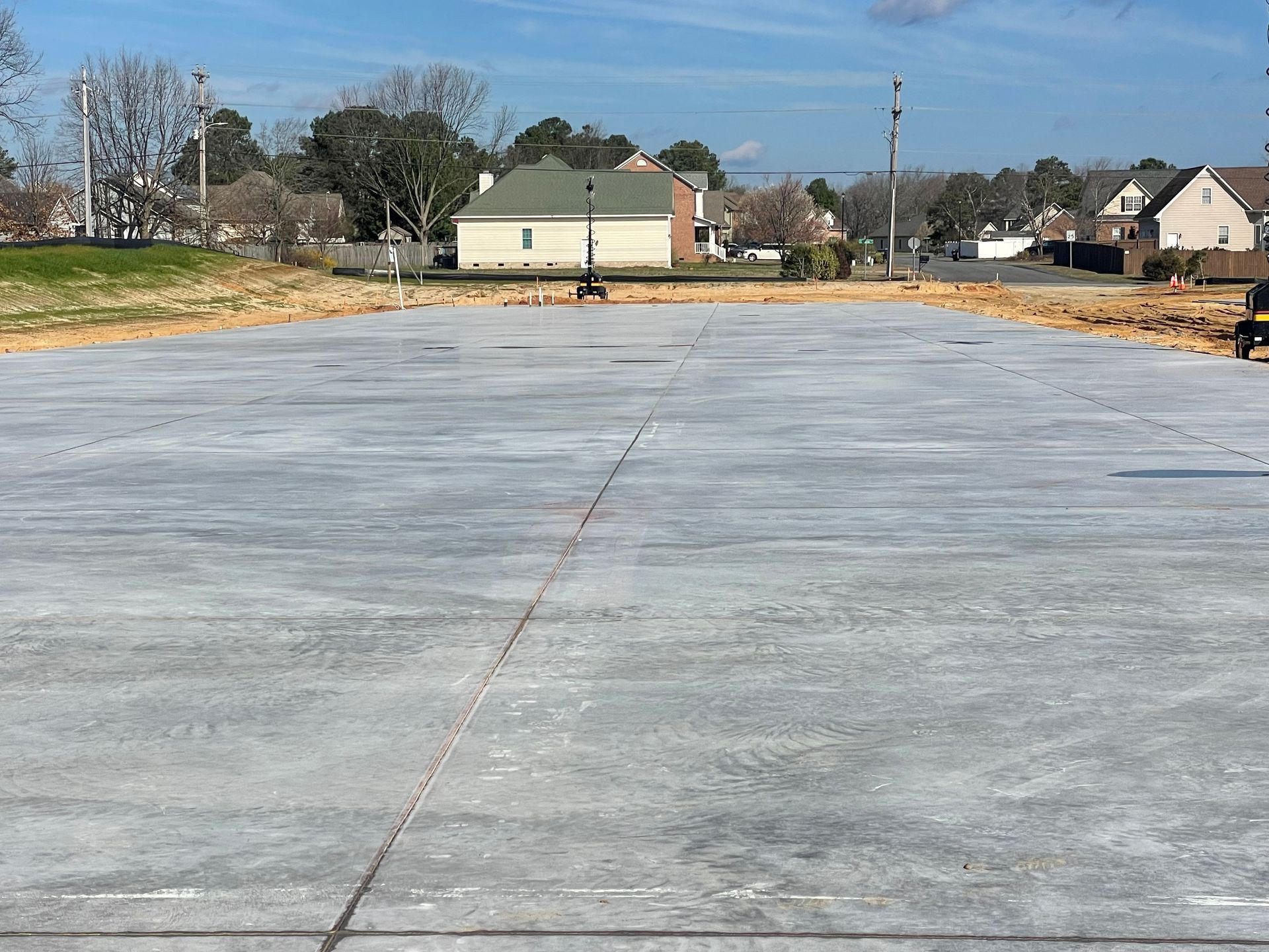 A large concrete parking lot with a house in the background.