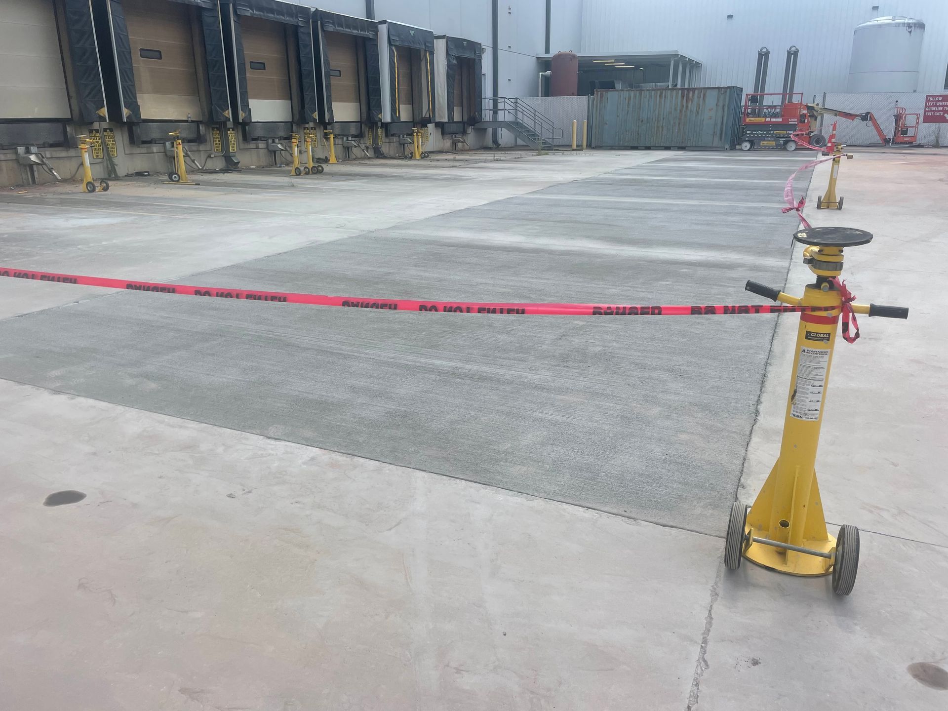 A yellow jack is sitting on a concrete surface in front of a warehouse.