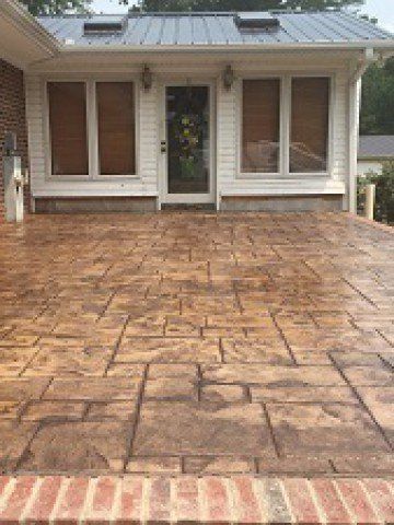 A concrete patio in front of a house with a brick border.