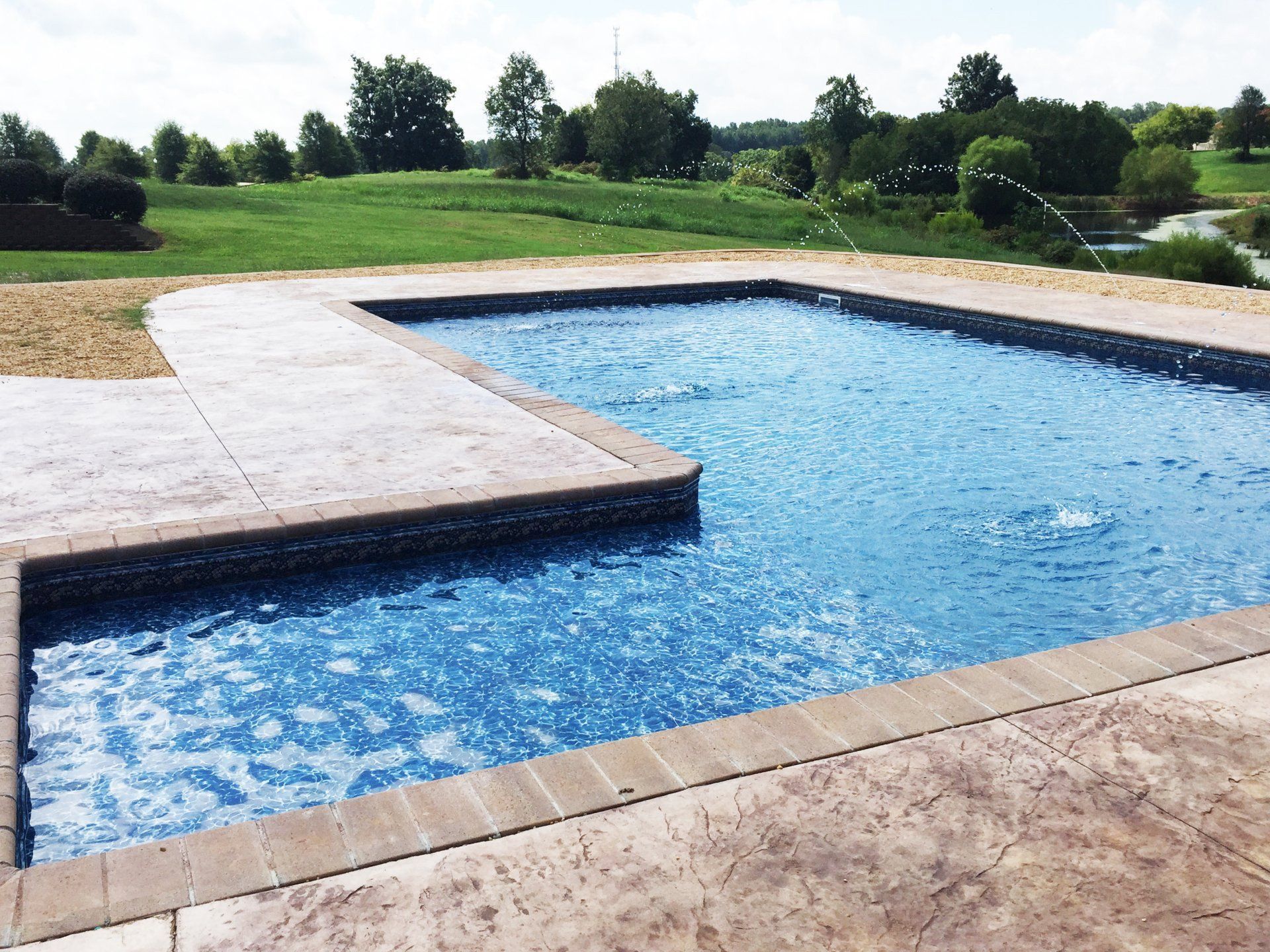 A large swimming pool with a fountain in the middle and a golf course in the background.