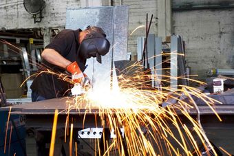 A man wearing a welding mask is grinding a piece of metal