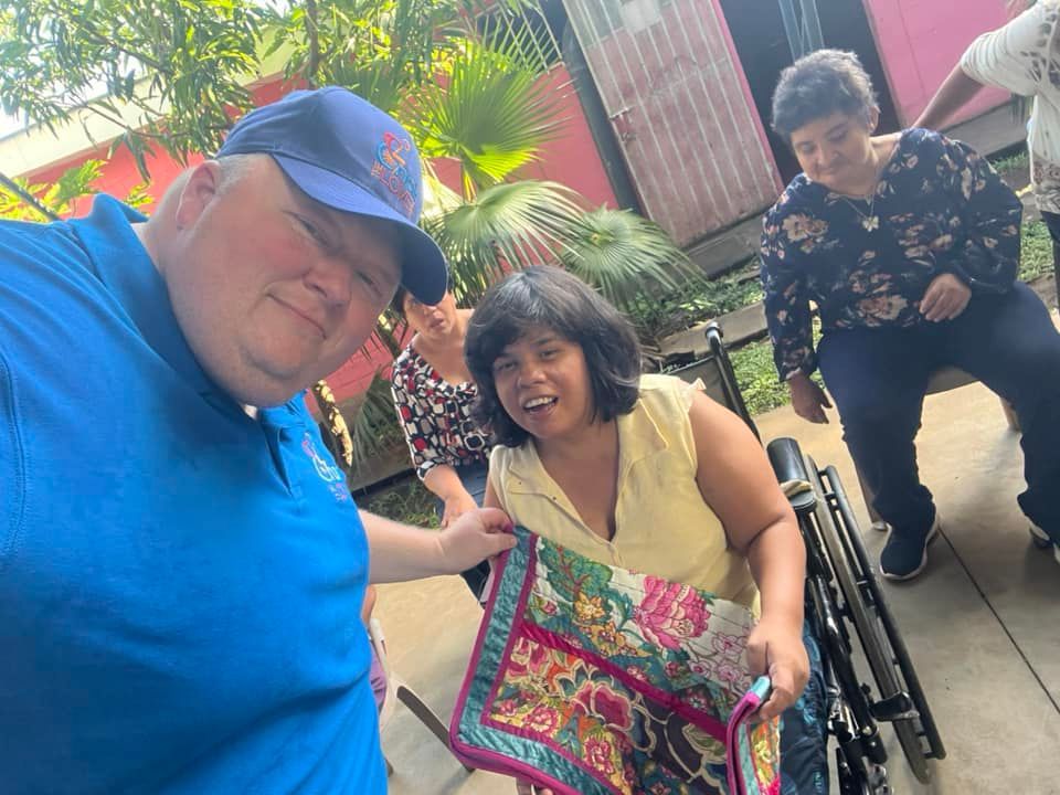 A man in a blue shirt is standing next to a woman in a wheelchair.