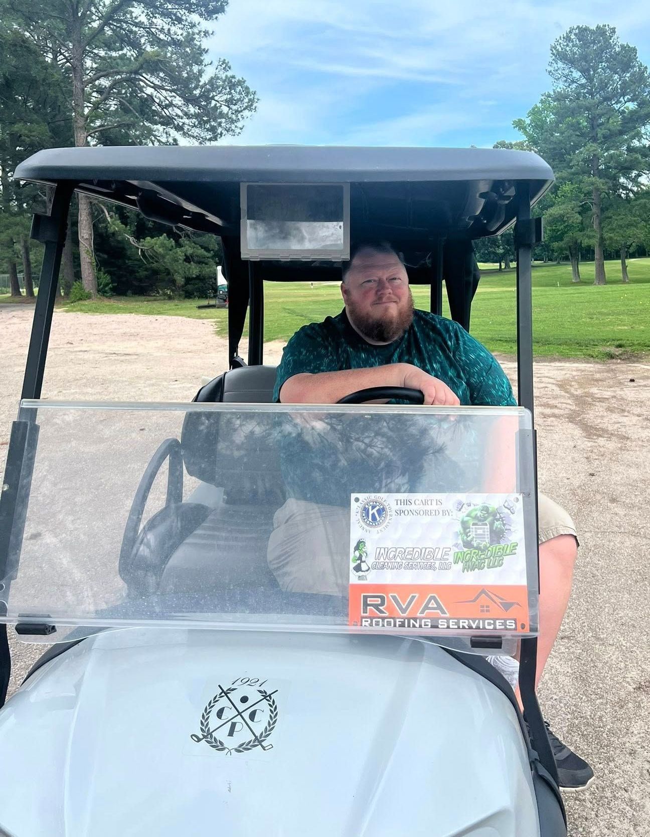 A man is sitting in a golf cart with a sticker on the windshield that says RVA Roofing Sevices