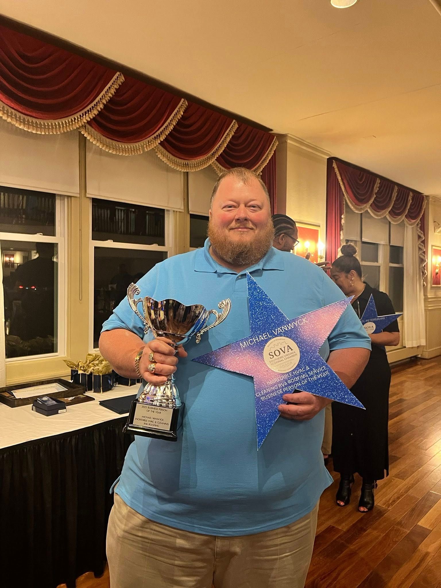 A man in a blue shirt is holding two trophies and a star.