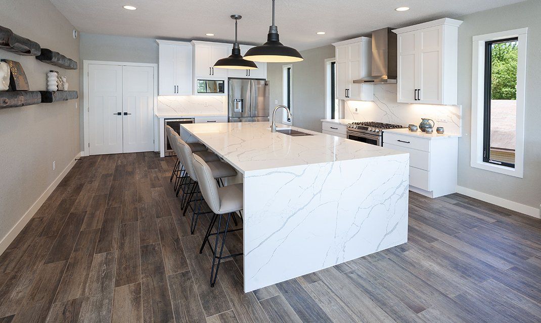 Modern kitchen with white cabinets, island, stainless steel appliances, and dark wood-look flooring.