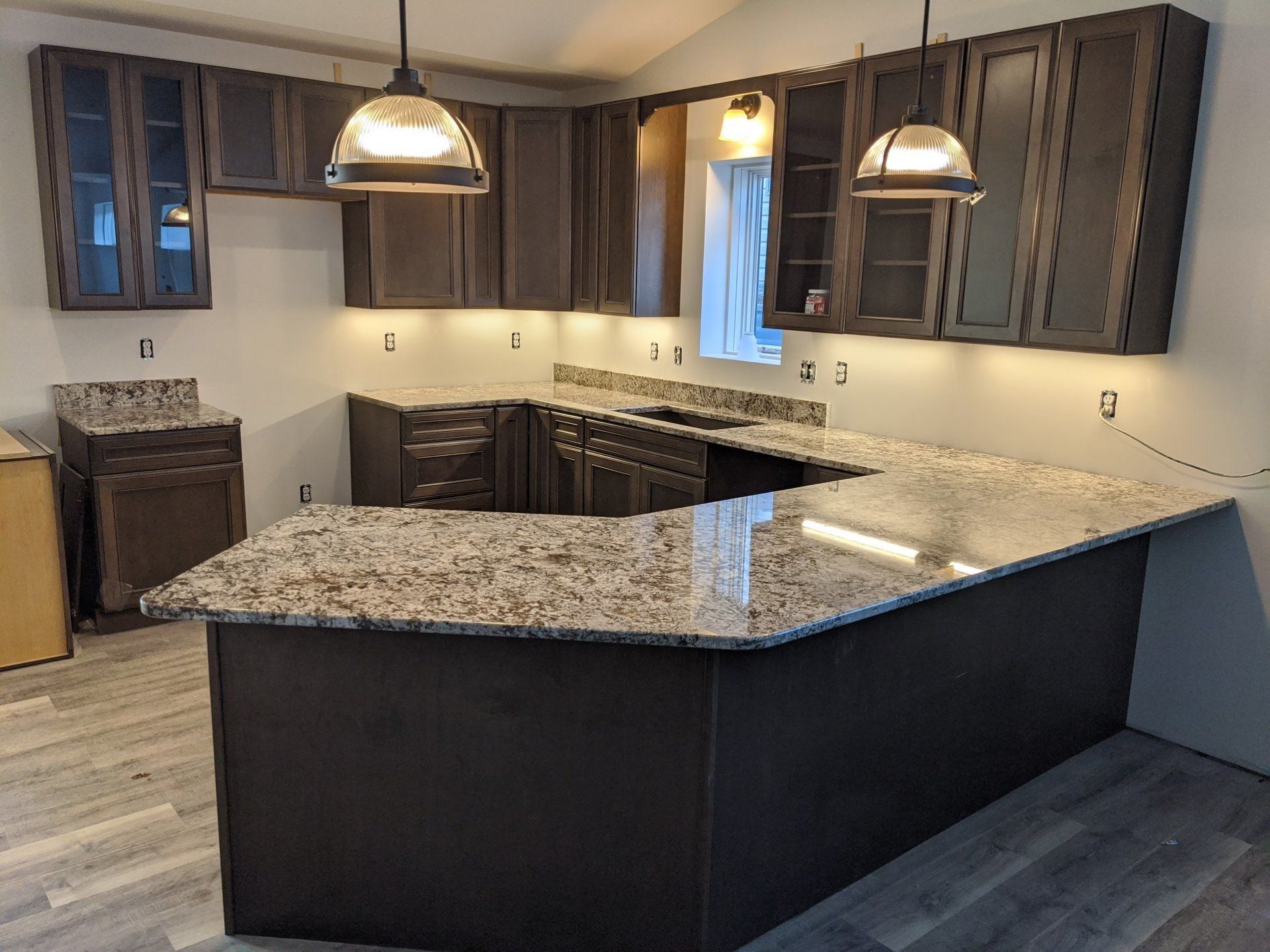 Dark-brown kitchen cabinets and countertops with two pendant lights. The kitchen is under construction.