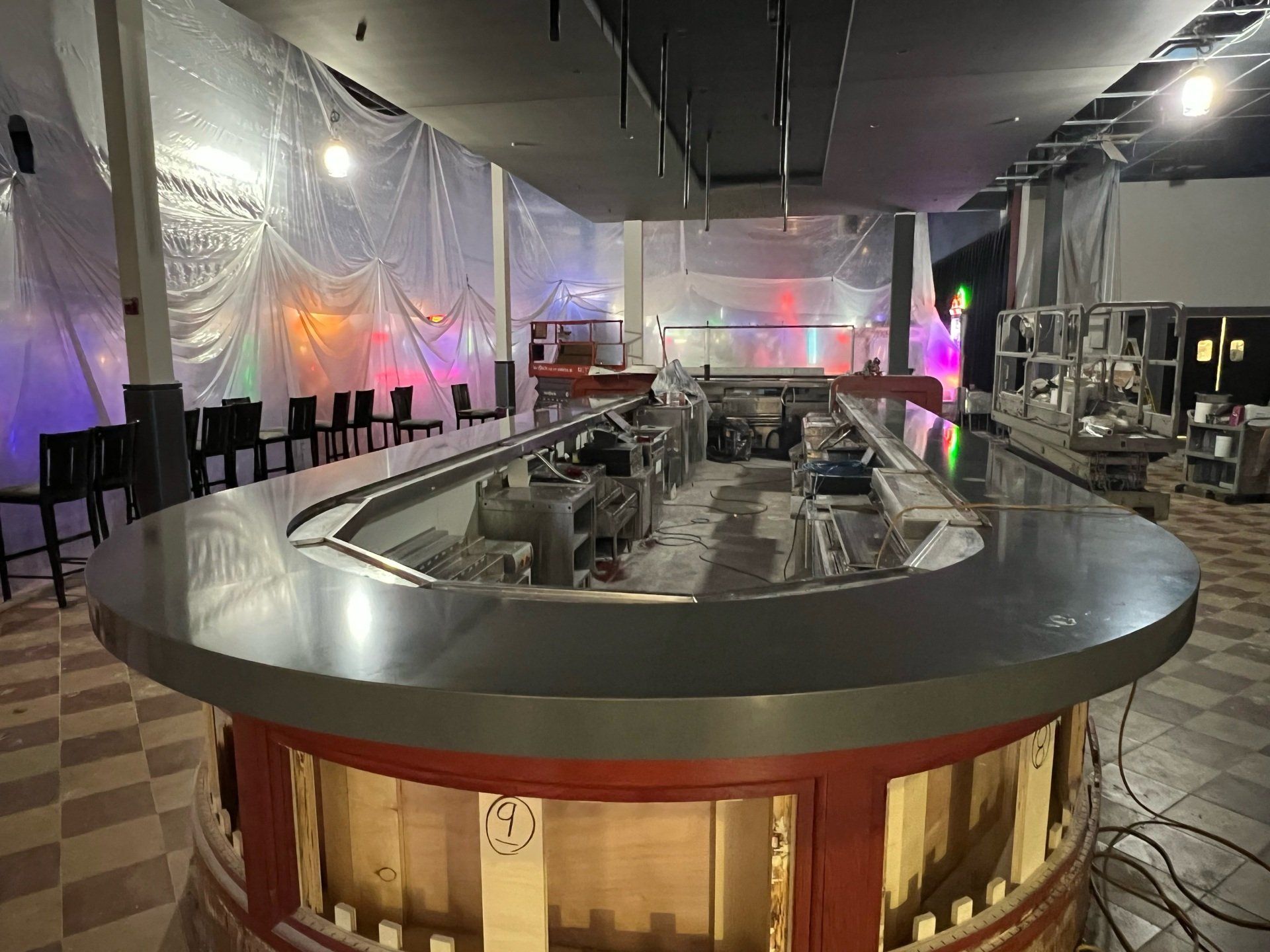 Bar under construction, curved stainless steel bar top, red base, plastic sheeting, exposed ceiling.