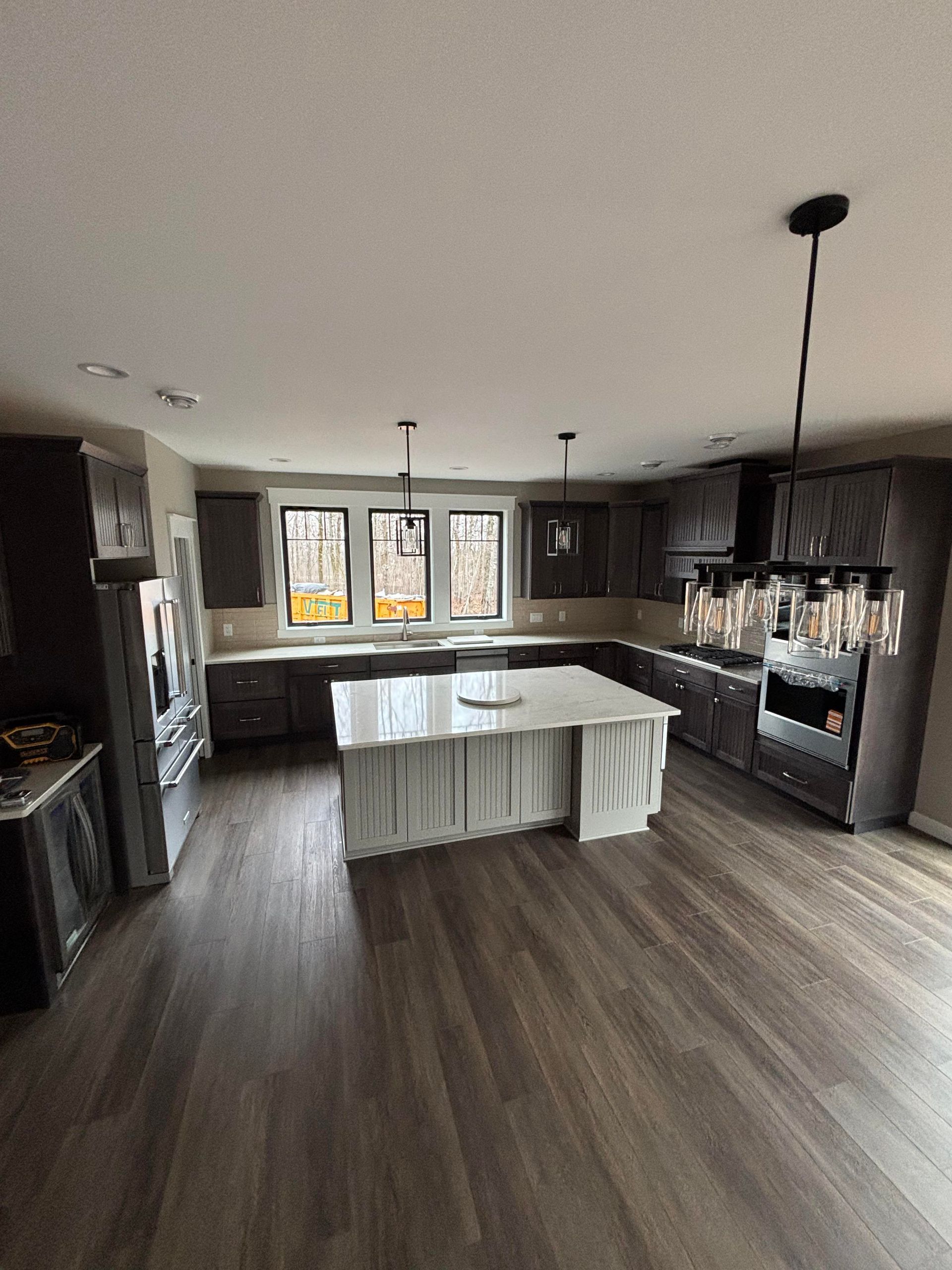 Modern kitchen with dark cabinets, wood floors, and a white island beneath pendant lighting.