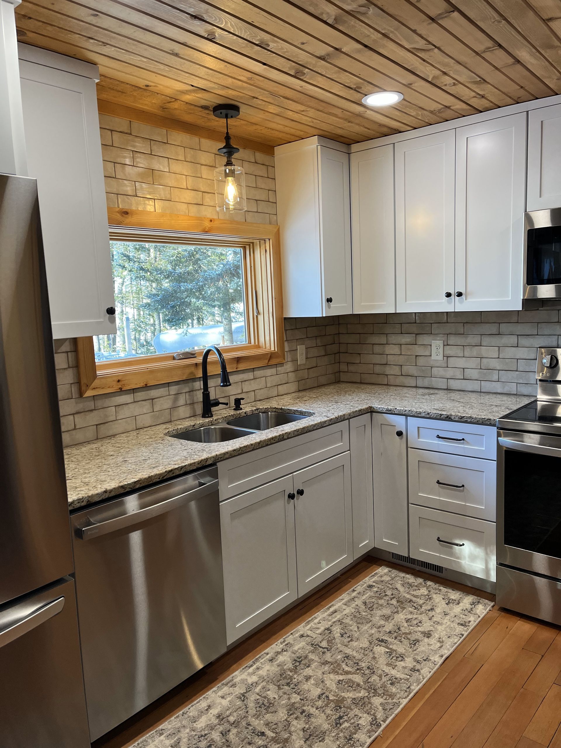 A kitchen with white cabinets, stainless steel appliances, granite counter tops, and a window.