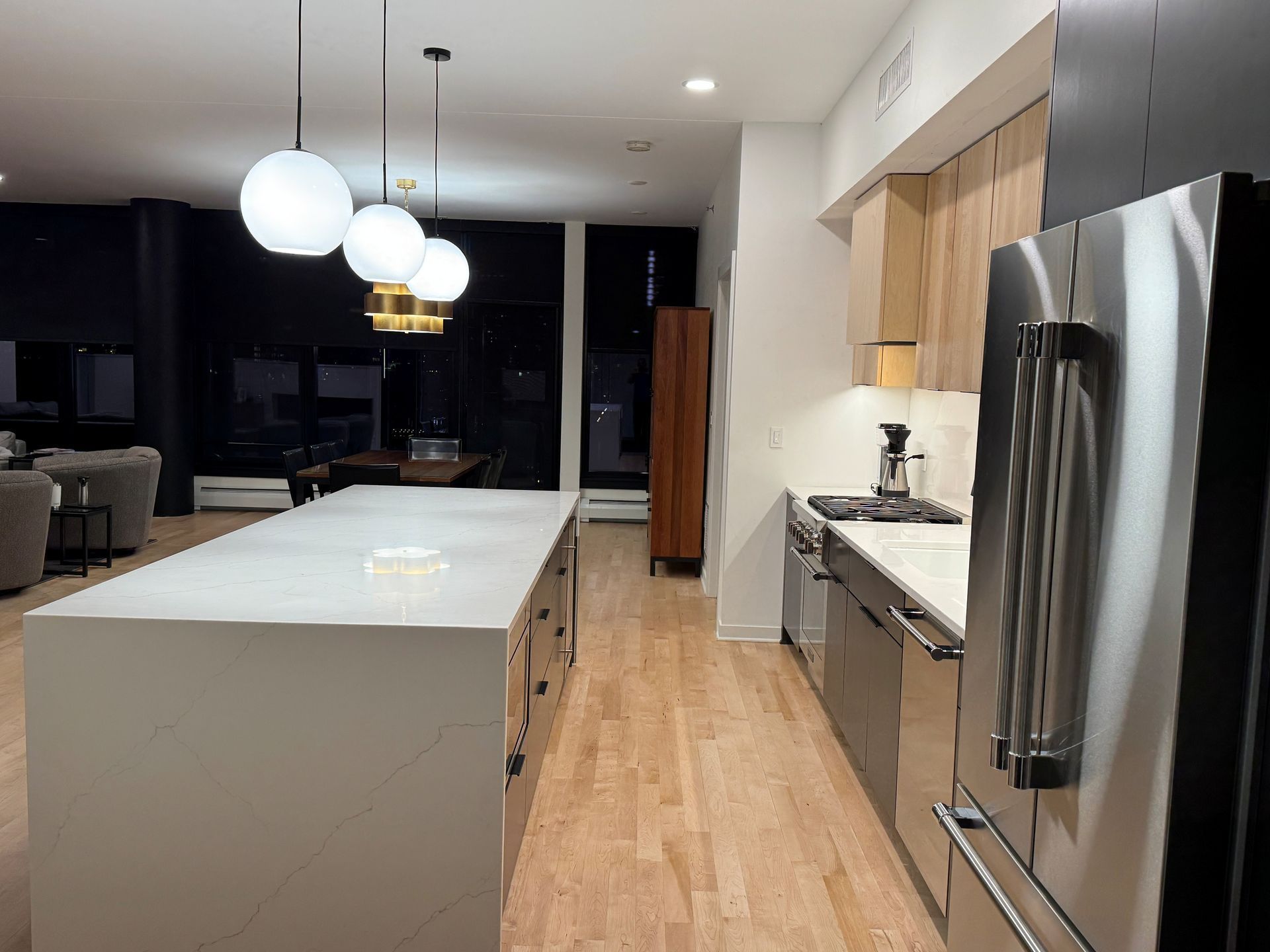 Modern kitchen with island, pendant lights, stainless steel appliances, and wood flooring.