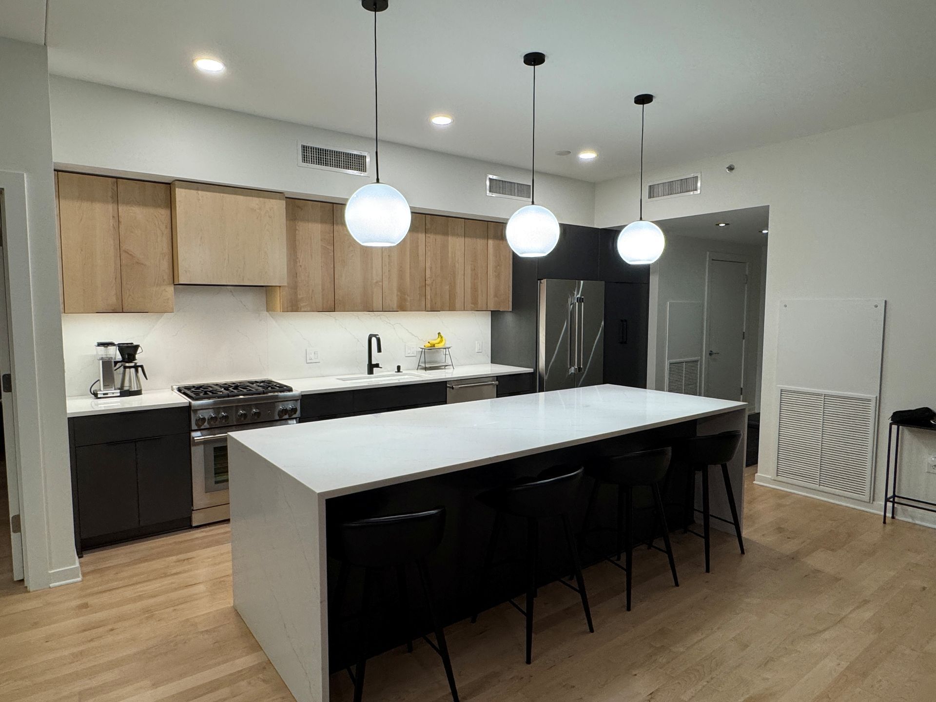 Modern kitchen with island, countertops, wooden cabinets, and globe pendant lights.