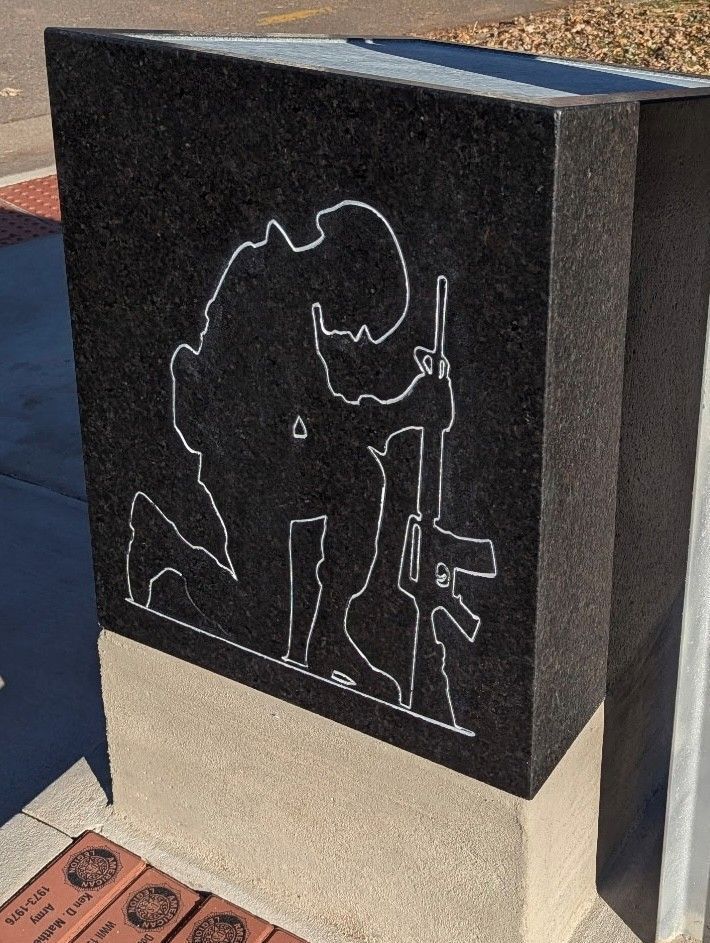 Silhouette of a kneeling soldier with a rifle, etched in white on a black granite monument.