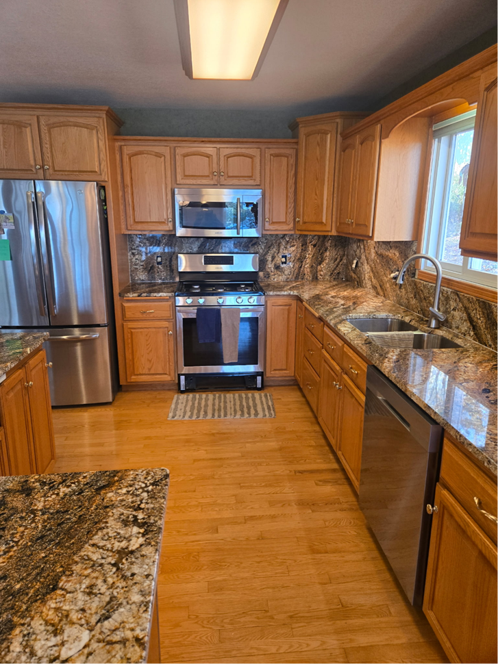 A kitchen with light-brown cabinets, stainless steel appliances, granite countertops, and hardwood floors