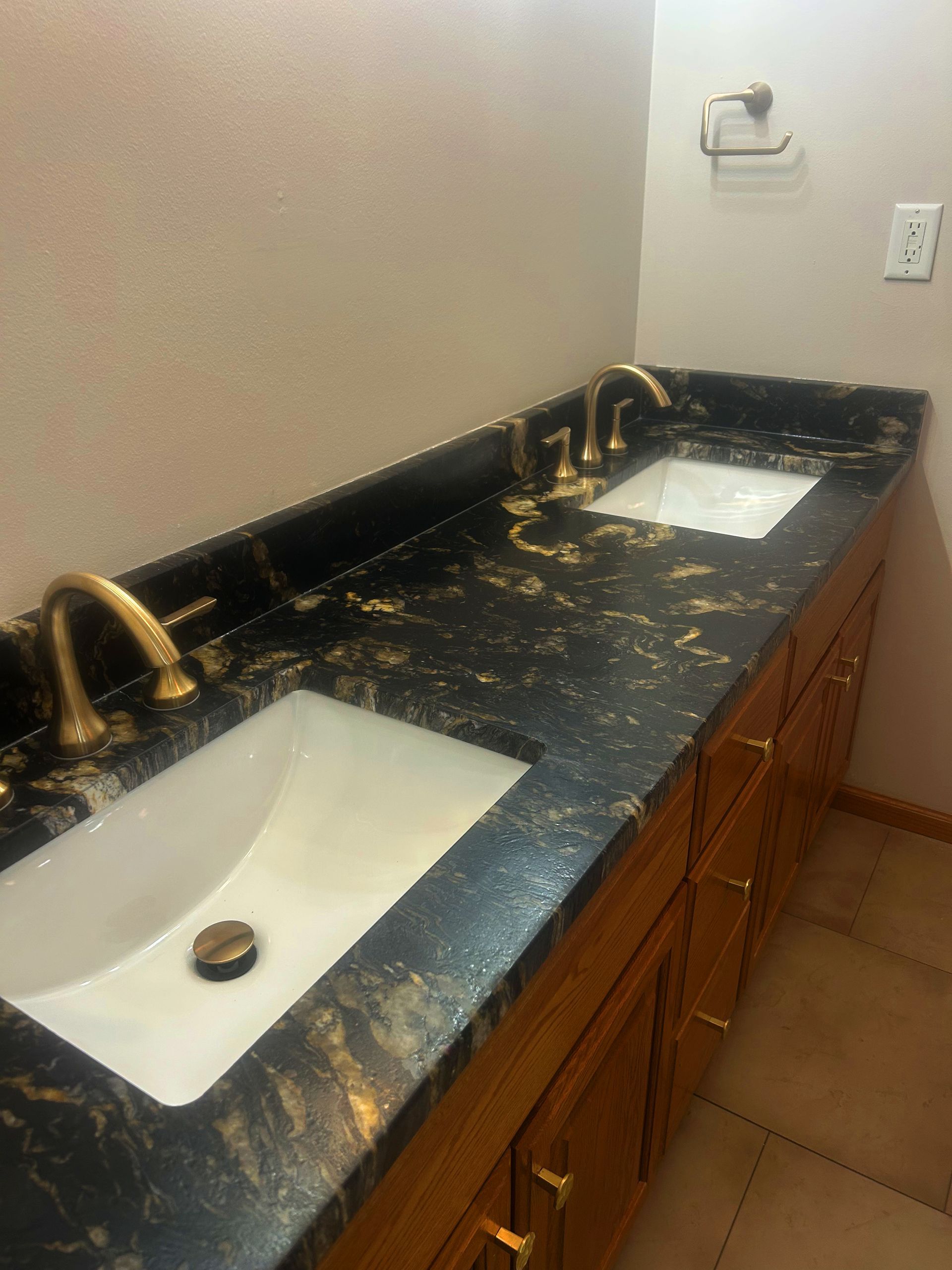 Double vanity with black speckled countertop and brass fixtures in a bathroom.