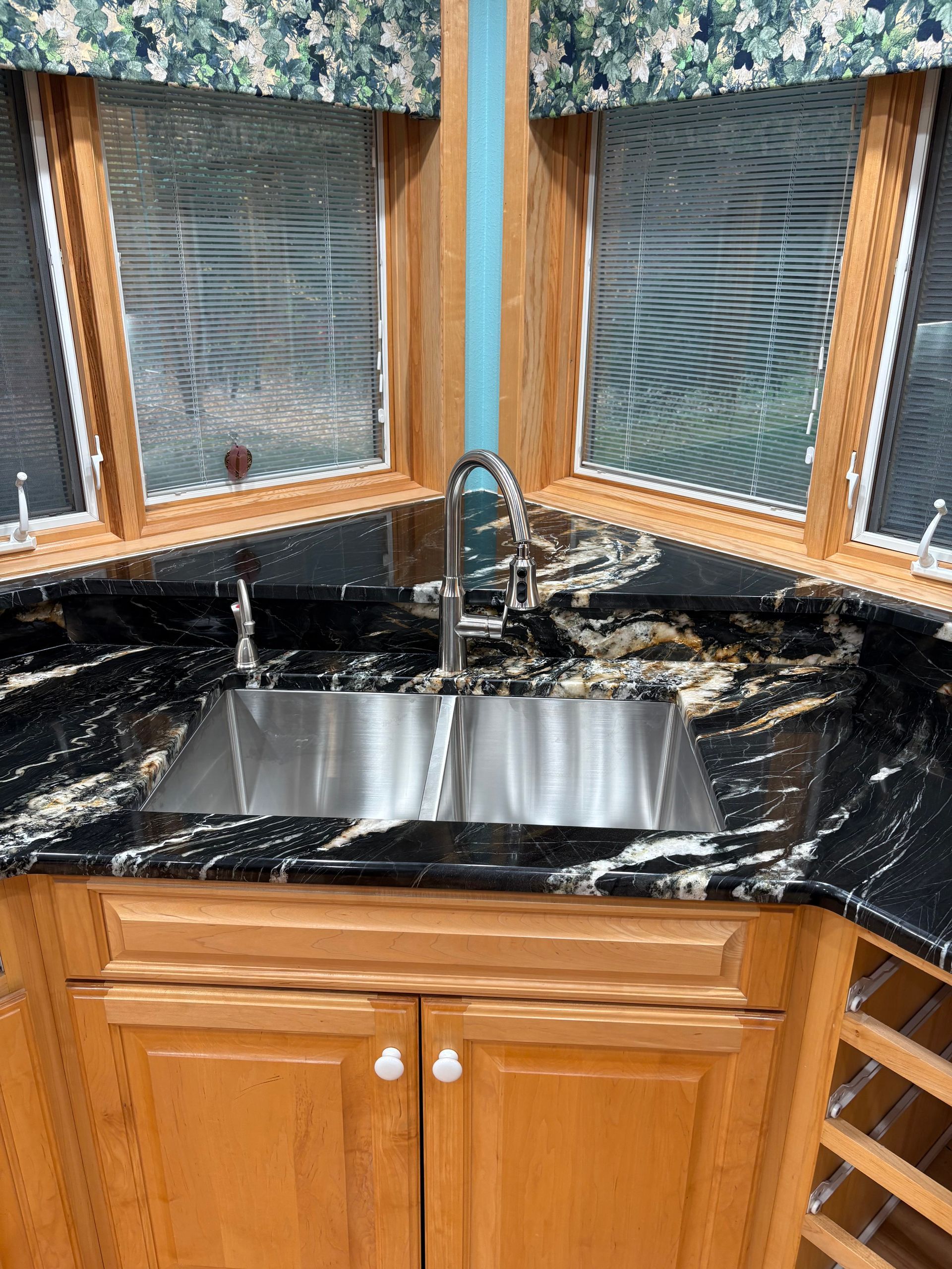 Stainless steel sink in a kitchen corner with black granite countertops and wooden cabinets.