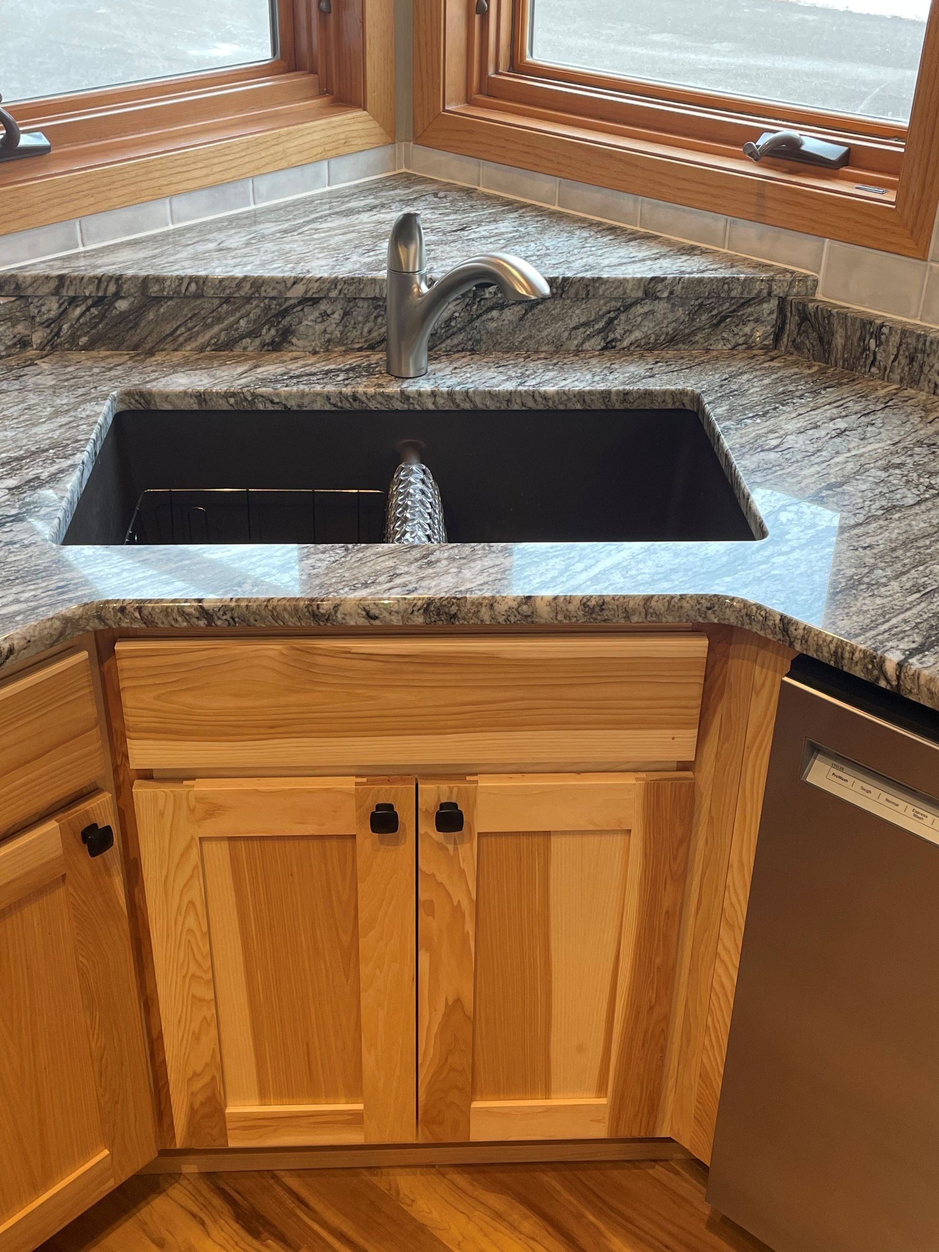 Kitchen corner with granite countertop, double sink, wood cabinets, and faucet.