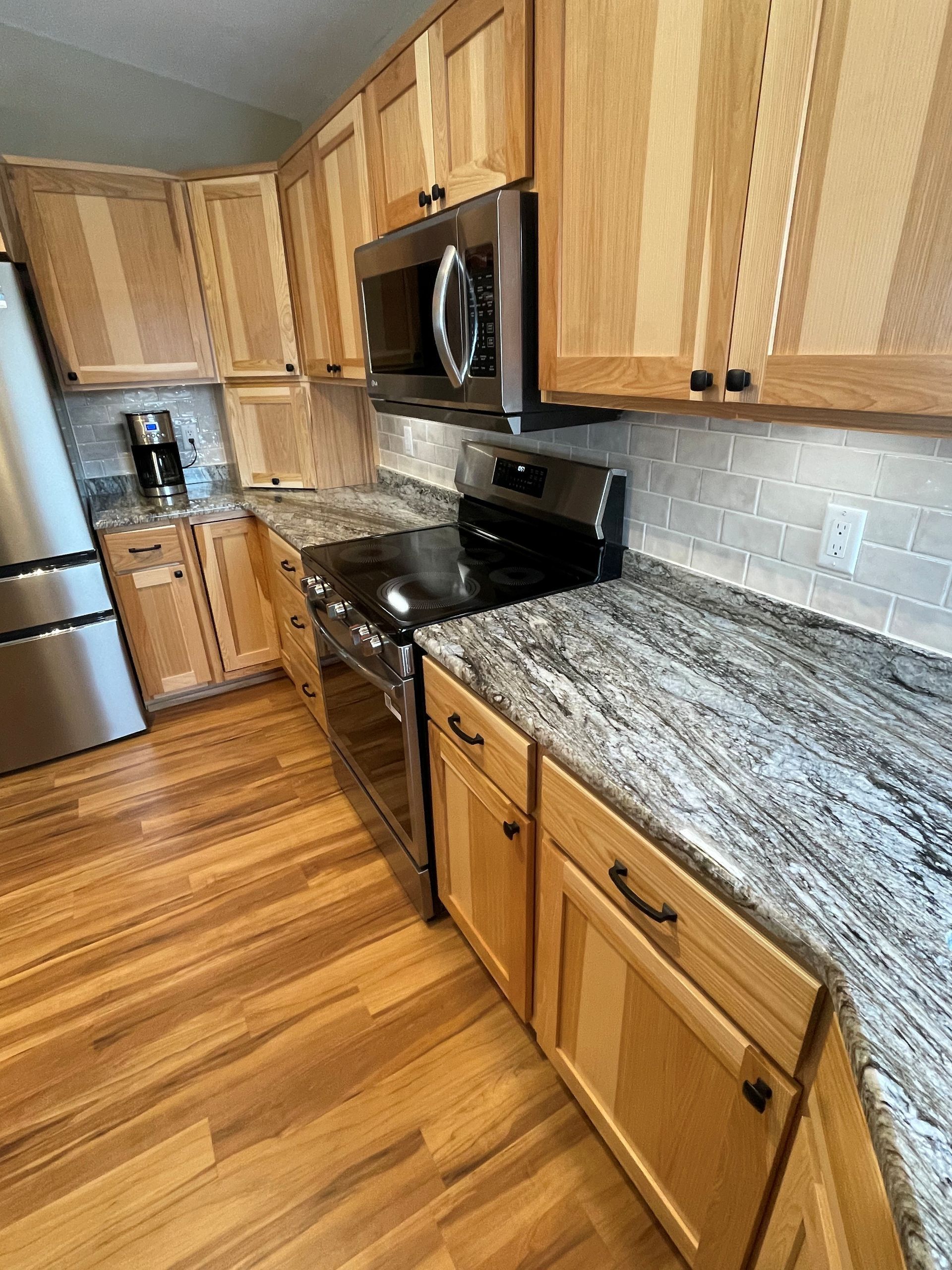 Kitchen with light wood cabinets, granite countertops, stainless steel appliances, and tiled backsplash.