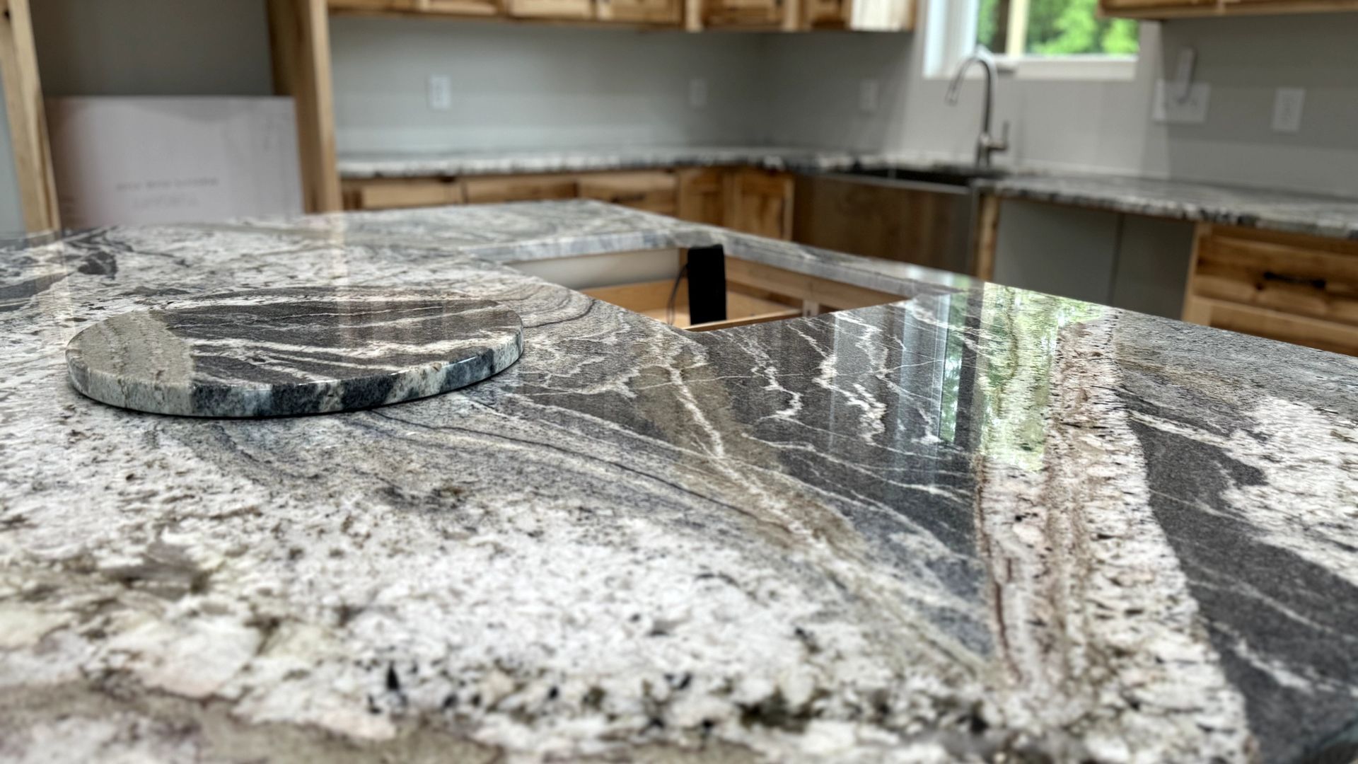 Close-up of a granite kitchen countertop with a round granite trivet. The countertop is light gray with dark gray and black veining.