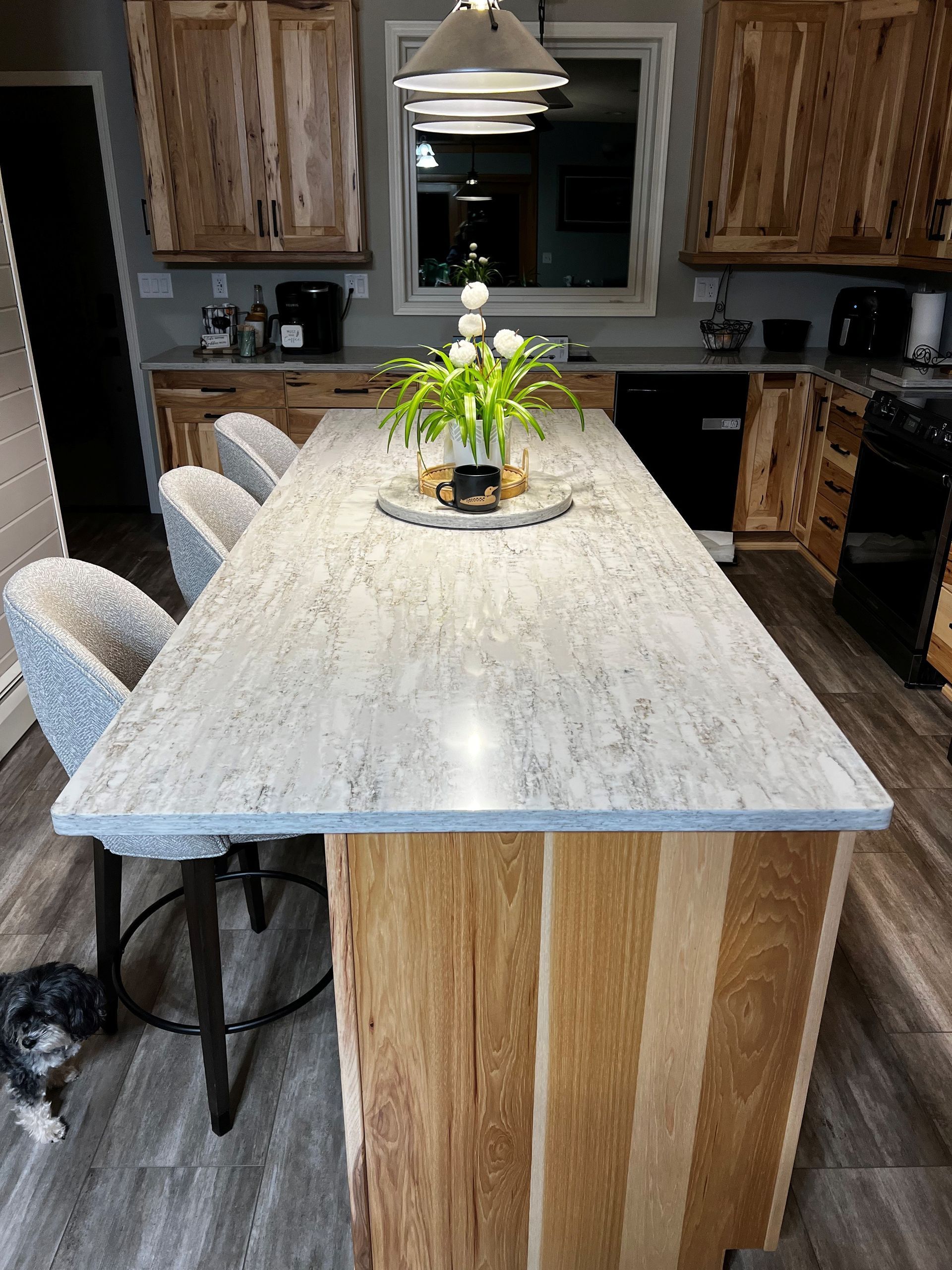Kitchen with wood cabinets and island, granite countertop, bar stools, dog on floor, and flowers.