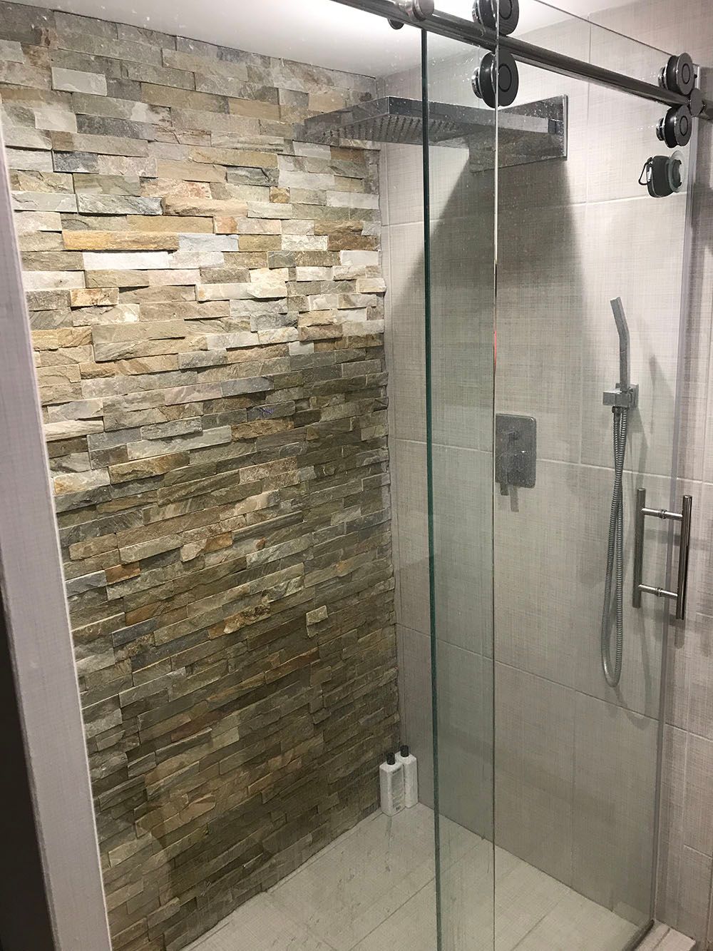 A bathroom with a sliding glass shower door and a stone wall.