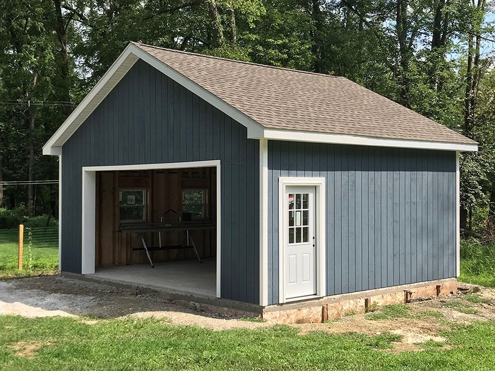 A blue garage with a brown roof is sitting in the middle of a lush green field.