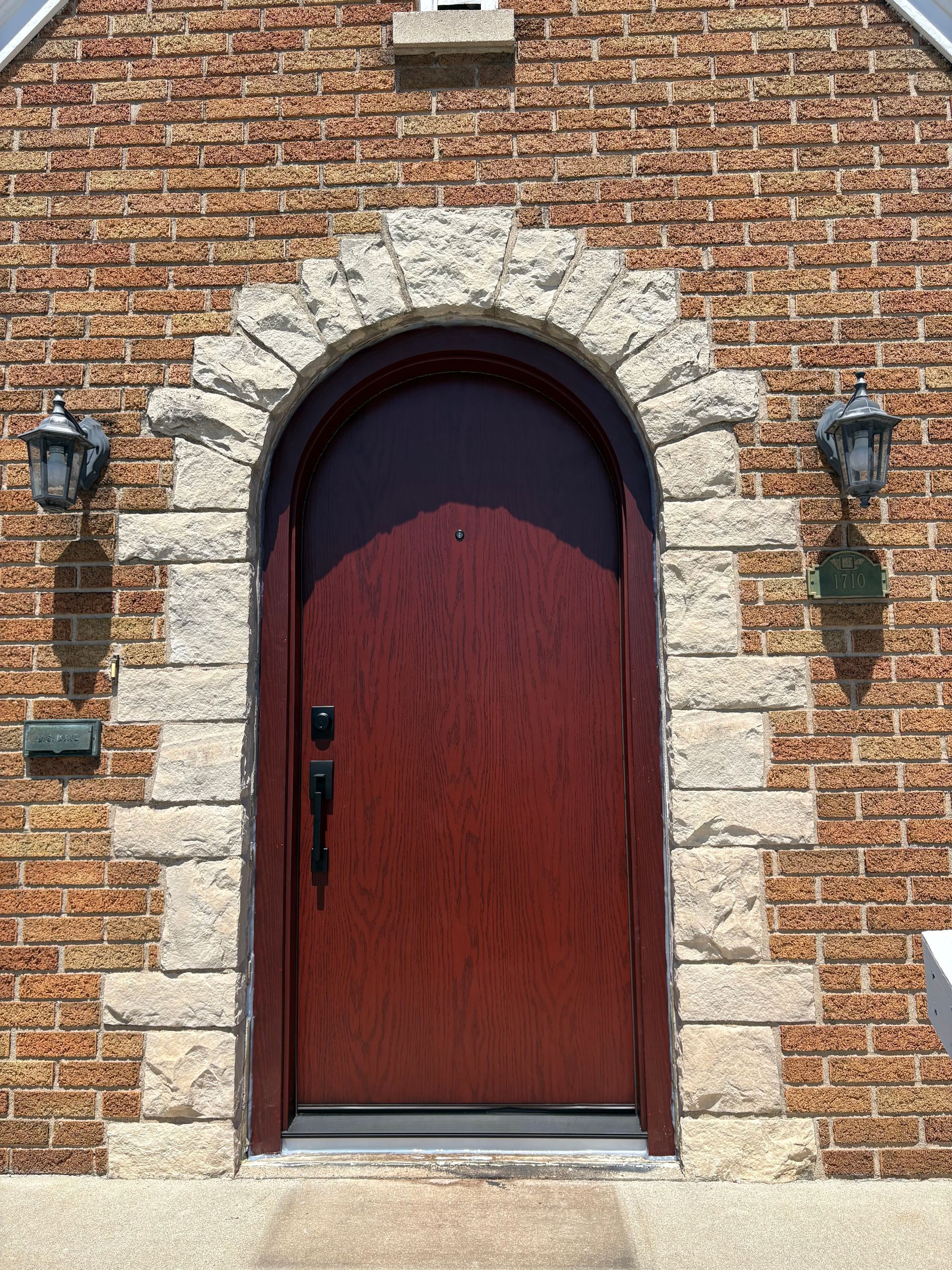 Brick house entrance with arched red door, white railings, and flower pots by the front steps