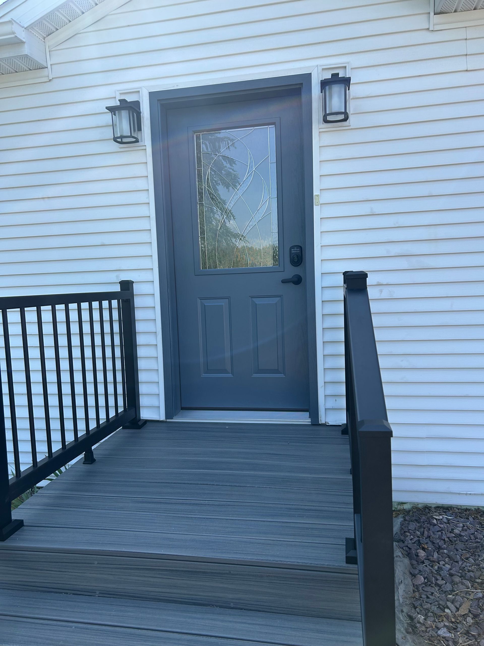 Front porch with gray door, black railings, and white siding on a house.