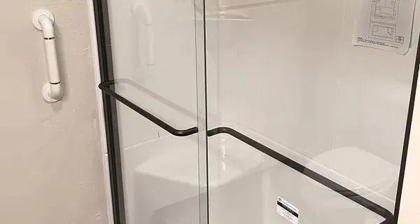 Shower with a white seat and grab bar. Glass door with black handle.