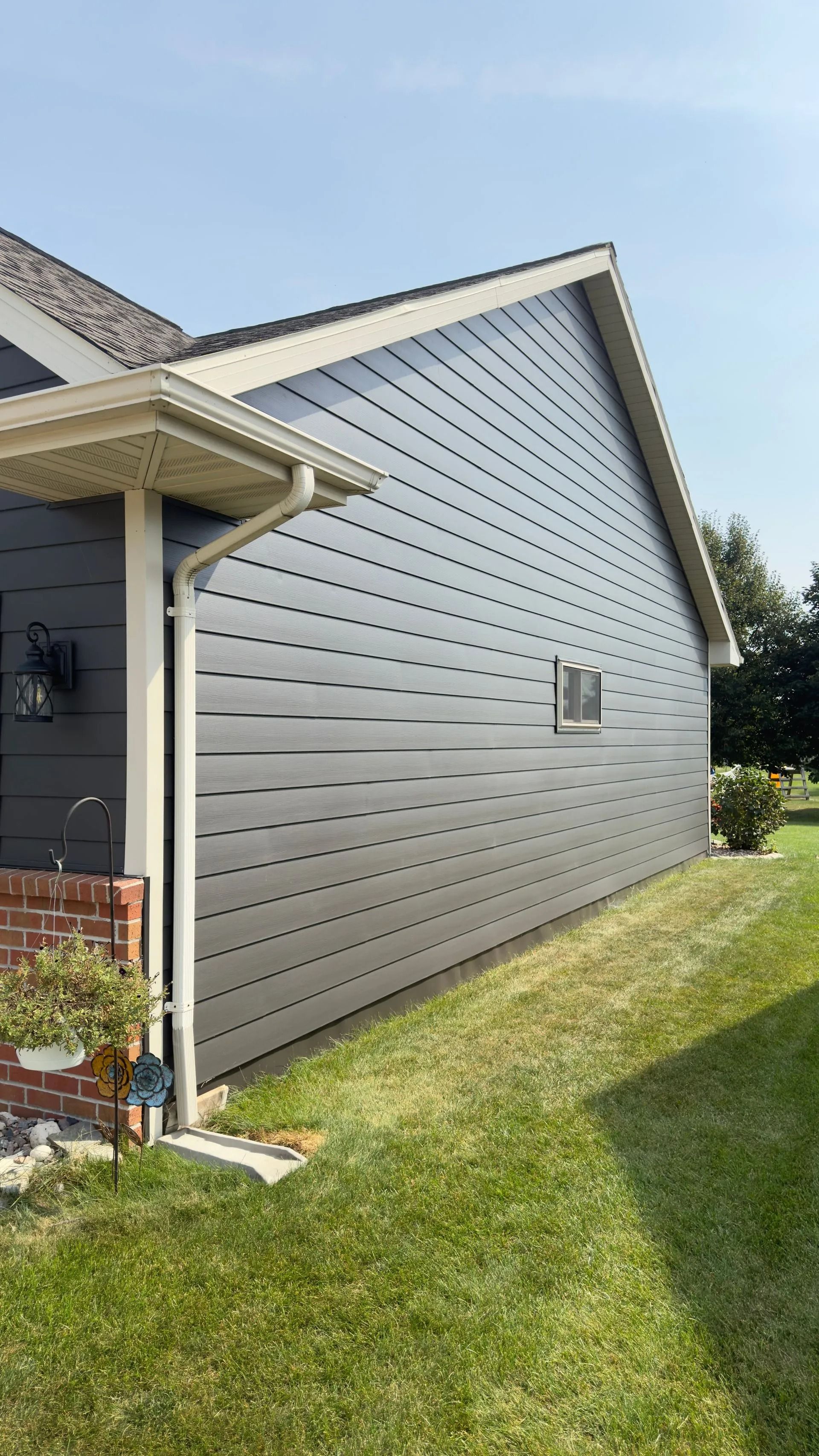 Gray siding on a house with beige trim, gutter, and roof. A small window is visible.