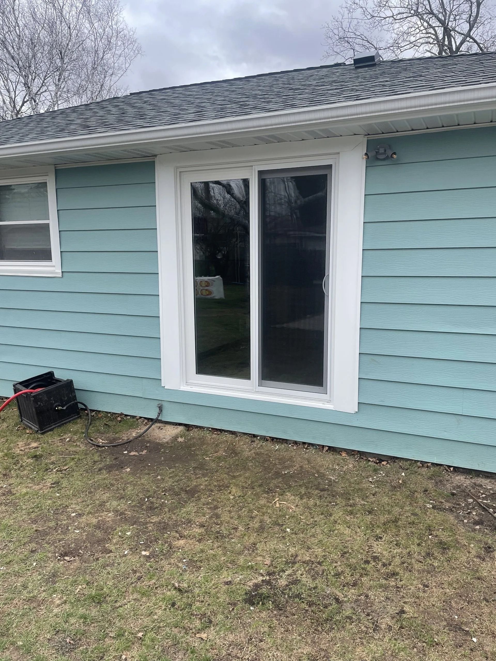 Sliding glass door on a light blue house with white trim. The yard has brown grass.