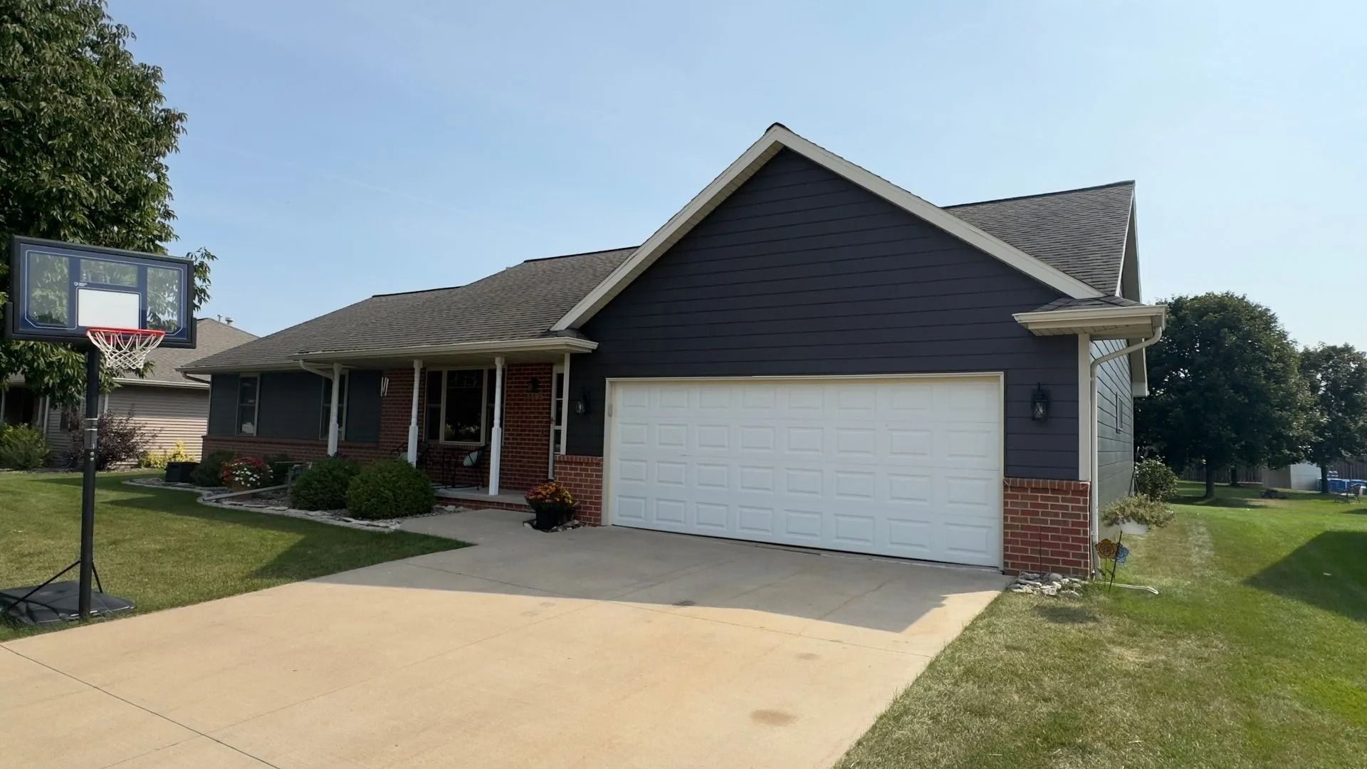 Blue-sided ranch house with white garage door and concrete driveway. Basketball hoop in front yard.
