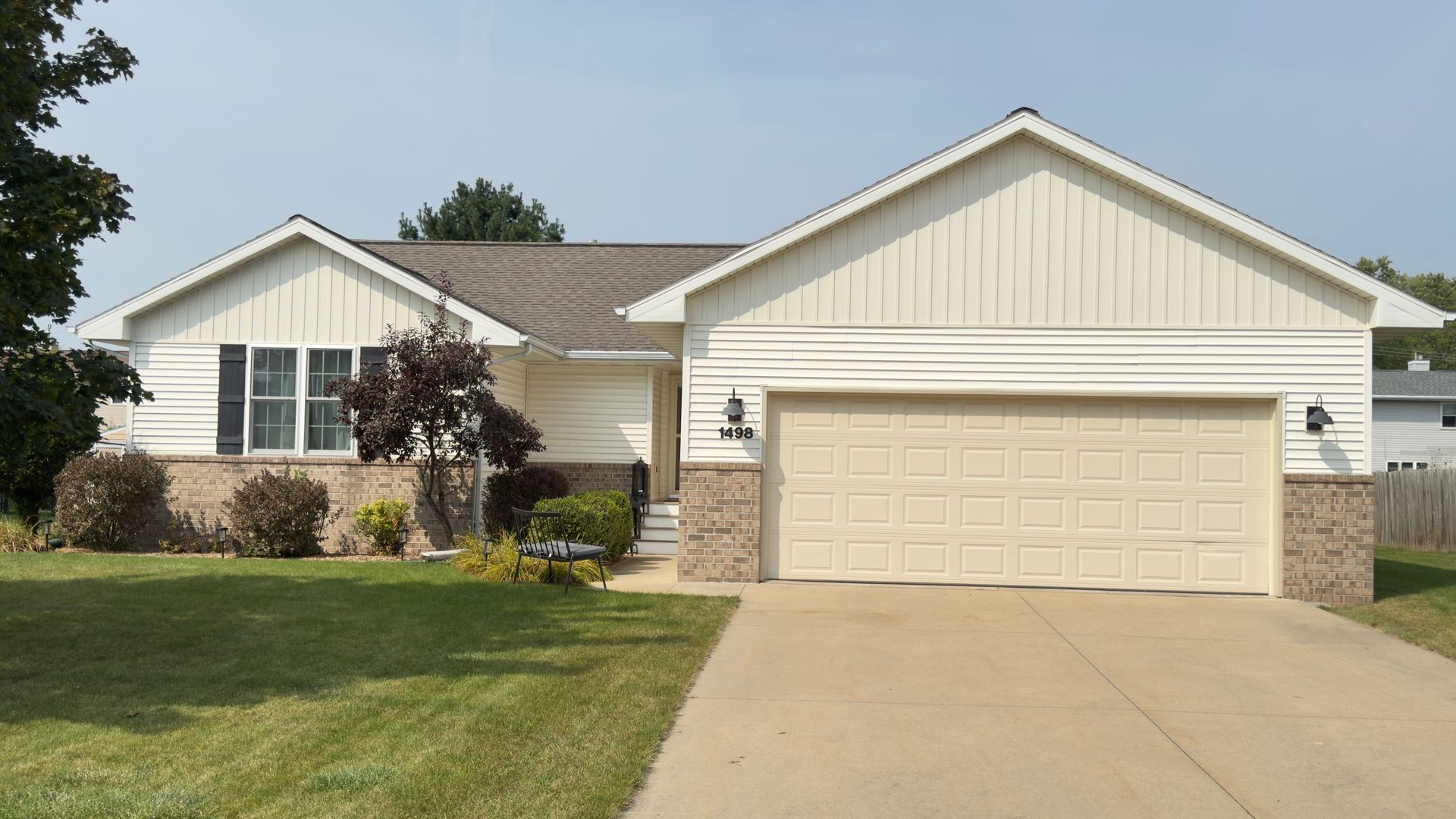 Beige ranch house with attached garage, tan siding, and brown roof under a blue sky.